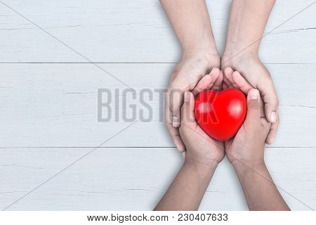 Love Mom Concept : Woman Holds Her Young Kids Hands Supporting Red Heart On Brown Wooden Table. Free