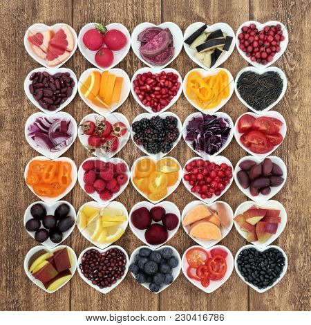 Anthocyanin health food concept with fruit, vegetable, pulses and grains in heart shaped bowls on rustic background.  Foods very high in anthocyanins, anthocyanins, vitamins and minerals.