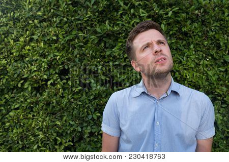 Successful Young Caucasian Man Looking To The Side Suspiciously On Green Tree Background. Concept Of