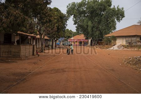 Nhacra, Republic Of Guinea-bissau - January 28, 2018: A Young Boy Playing With An Old Tire In A Dirt