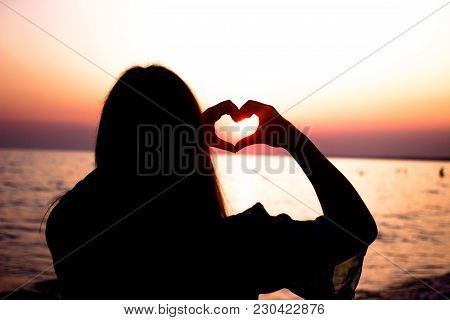 Heart Symbol Made With Two Hands. Girl In Love Enjoying Tender Moments At Sunset During Holiday With