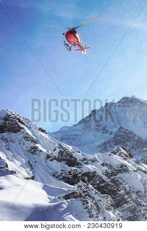 Red Helicopter Flying Above Swiss Alpine Mountain Mannlichen In Winter, Switzerland
