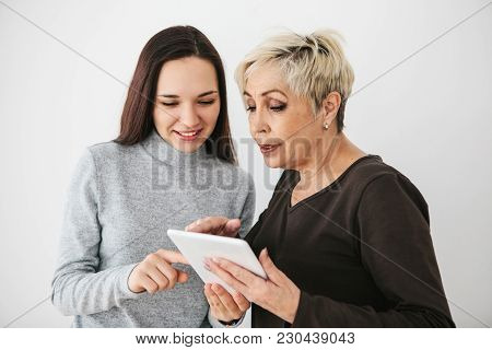 A Young Girl Volunteer Or Granddaughter Explains To An Elderly Woman How To Use A Tablet Or Shows So