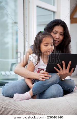 Mutlu anne ve kızı CRI alanıyla ev iç, sığ derinlikte yapılan dijital tablet kullanma