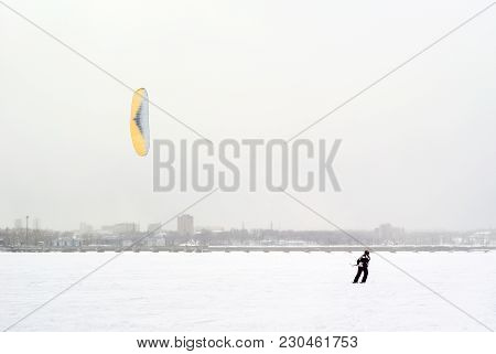 Snow Kiter Rides On The Ice Of A Frozen Lake Against The Background Of The City During A Snowfall