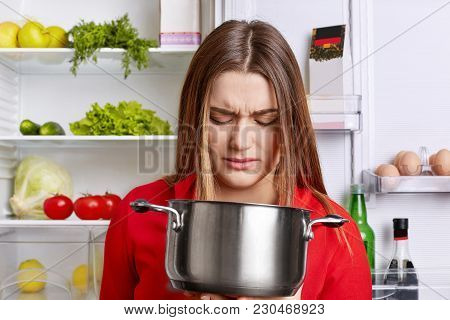 Angy Displeased Female Housewife Looks In Pot With Foul Meal, Smells Unpleasant Stink, Stands Near F
