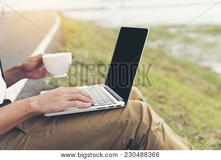 Smart Man Working On Laptop And Holding A Cup Of Coffee Outdoor On The Road. Business Concept.