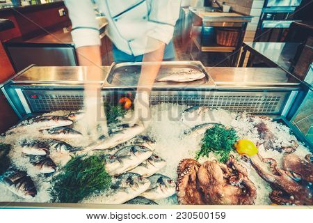 The chef-cooker is taking the freshly caught fish out of the refrigerated counter for the cooking delicious meal in the restaurant. Fresh seafood the fish and octopuses for healthy lifestyle.