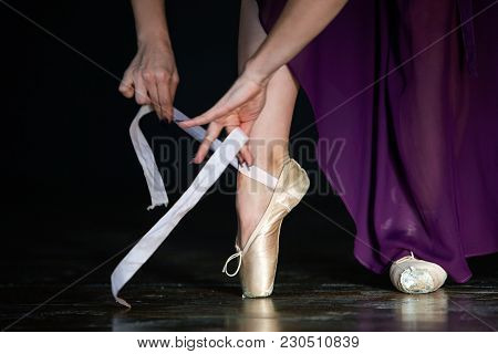 Elegant Ballerina In Light Satin Purple Training Skirt Is Posing In The Studio On The Dark Backgroun
