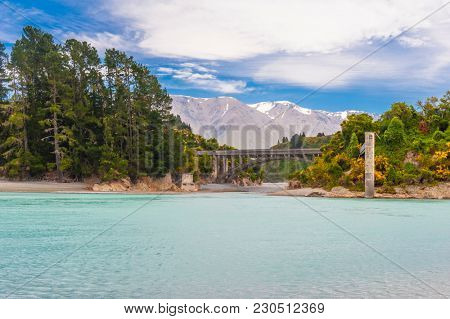 Bridge over river Rakaia with a view at Southern Alps peaks, turquoise river and blooming yellow gorse