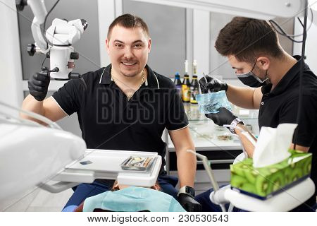 Male Dentist With Ceramic Braces Is Smiling To The Camera While Another Is Working With Medical Inst