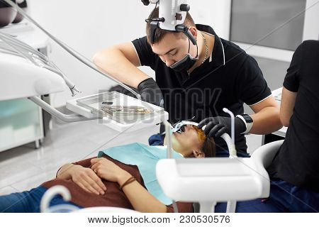 Male Dentist In Black Uniform Fixing Young Girl Teeth With Dental Instruments