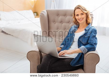 Pleasant Day. Cheerful Positive Smiling Woman Being In Her Comfortable Light Clean Bedroom And Feeli