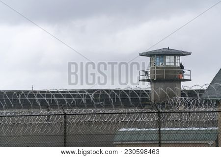 An Armed Guard Surveys The Grounds From The Railing Of A Prison Watchtower