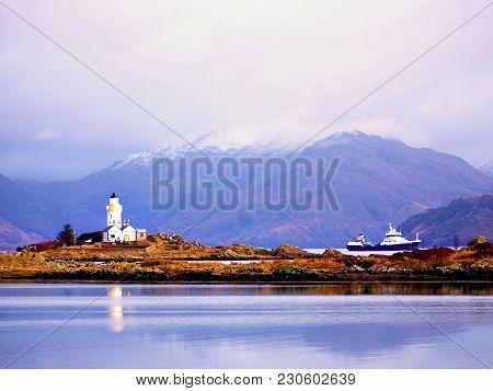 Famous Isle Ornsay With  Lighthouse Tower, Isle Of Skye, Scotland, Uk. Snowy Mountains In Background