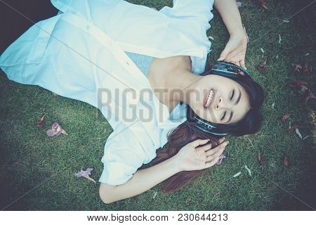 Young Woman Lying On Grass Floor Listening Music From Moblie Phone With Headset. Girl Chilling Lifes
