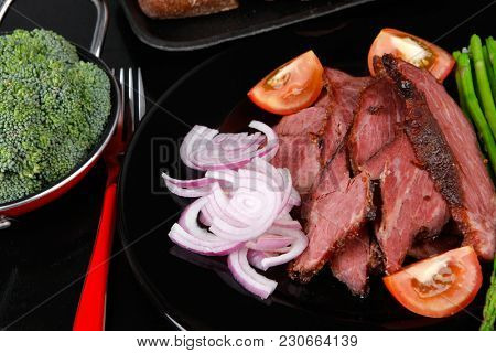 business lunch fresh roast beef meat slices on black plate wotj cutlery asparagus boiled broccoli rye bun on wooden table