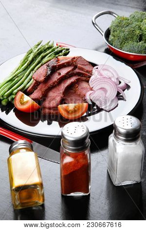 business lunch fresh roast beef meat slices on black plate wotj cutlery asparagus boiled broccoli rye bun on wooden table