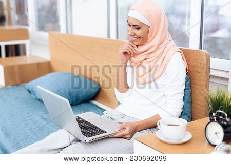 An Arabian Woman Is Drinking Tea And Working On The Computer While Sitting On The Bed. She Rests At 