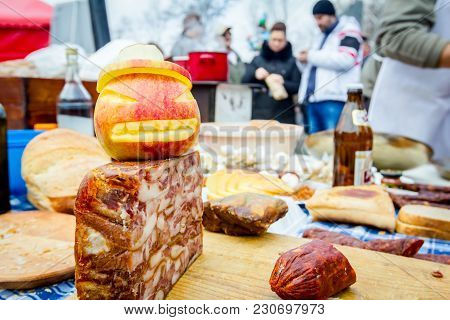 Headcheese And Smoked Sausage On A Wooden Chopping Board At Outdoor Kitchen, People In Background Ar