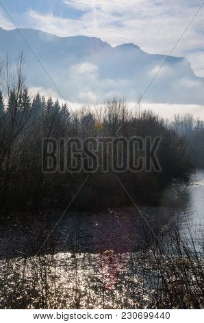 Tree-filled River Banks Near The Town Of Echelles, In The French Savoy Eary, On A Dramatically Cloud