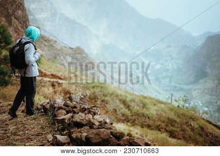 Traveler With Backpack Staying On The Edge Of Path Leading Through Rural Landscape With Mountains, O