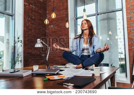 Female Student Sitting In Lotus Pose On Table In Her Room Meditating Relaxing After Studying And Pre