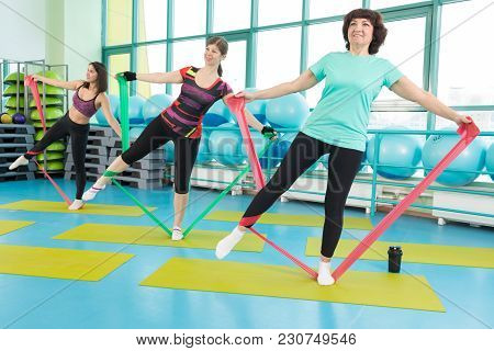 50-year Woman Doing Exercise With Latex Fitness Band During Workout In A Gym.