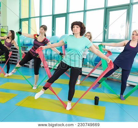 50-year Woman Doing Exercise With Latex Fitness Band During Workout In A Gym.