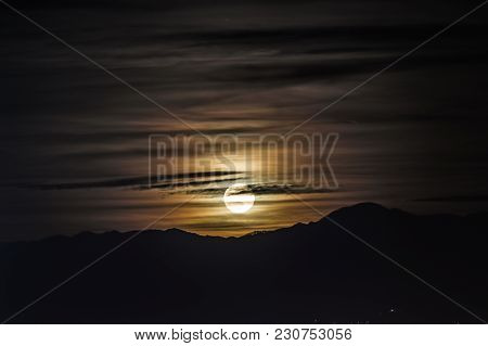 Night Scene - Full Moon Shining Brightly In The Sky With Clouds On Mountains Background.