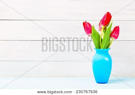 Colorful Red Spring Tulip Flowers In Nice Blue Vase On Light Wooden Background As Greeting Card. Mot