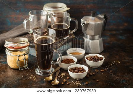 Coffee In Glass Cup, Coffee Beans, Ground Coffee And Brown Cane Sugar On Dark Background