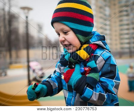 Active Little Boy Runs Around On The Playground And Has Fun. Beautiful Kid Smiling And Holding Toys 