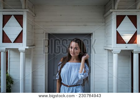 Young Inscrutable Woman Stands At The Entrance Of A Colonial Style Wooden White House. Beautiful Gir