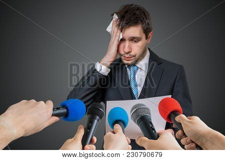 Nervous Man Is Afraid Of Public Speech And Sweating. Many Microphones In Front.