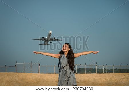 Female Traveler Is Standing On The Beach And Looking On The Aircraft. Jet Plane Takes Off On The Bac