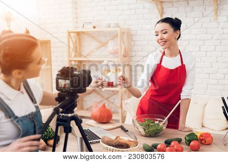 Two Culinary Bloggers In Red Aprons Tasting Winewith One Girl Behind Camera.
