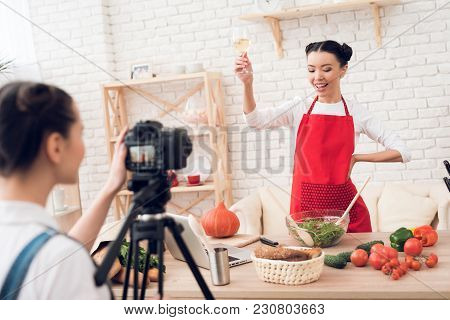 Two Culinary Bloggers In Red Aprons Tasting Winewith One Girl Behind Camera.