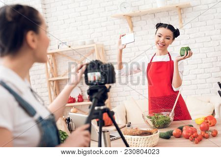 Two Culinary Bloggers In Red Aprons Taking Selfie With One Girl Behind Camera.