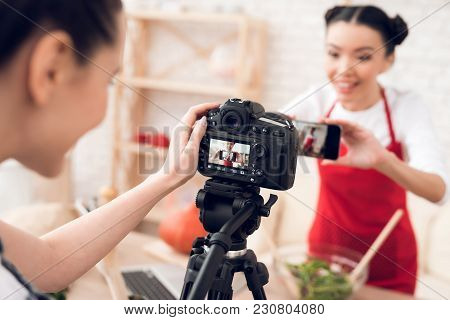 Two Culinary Bloggers In Red Aprons Taking Selfie With One Girl Behind Camera.