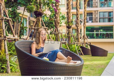Young Female Freelancer Sitting Near The Pool With Her Laptop In The Hotel Browsing In Her Smartphon