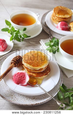 Two Portions Of Banana Pancakes With Honey And Fruit Sorbet And Cups Of Green Tea For Breakfast