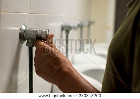 closeup of a young caucasian man flushing a urinal in a public washroom