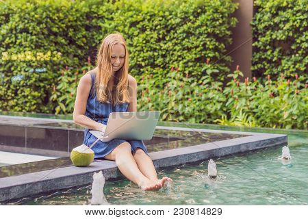 Young Female Freelancer Sitting Near The Pool With Her Laptop In The Hotel Browsing In Her Smartphon