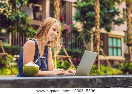 Young Female Freelancer Sitting Near The Pool With Her Laptop In The Hotel Browsing In Her Smartphon