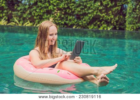Young Female Freelancer Sitting Near The Pool With Her Laptop In The Hotel Browsing In Her Smartphon