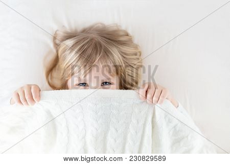 Little Girl Peeking Out Blanket On Bed. Cute Kid Smiling And Hiding Under Knitted Cover. Palyful And