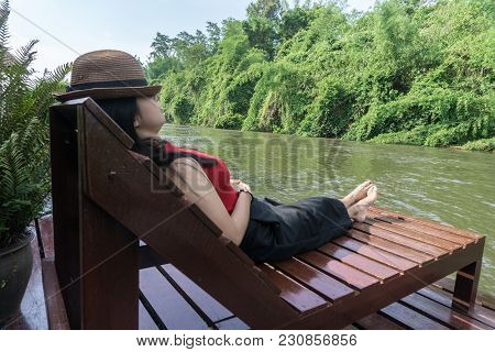 Asian Girl In The Resort In Red Clothes And Hat Sleep On Bed Pool., Background Of A Beautiful River.