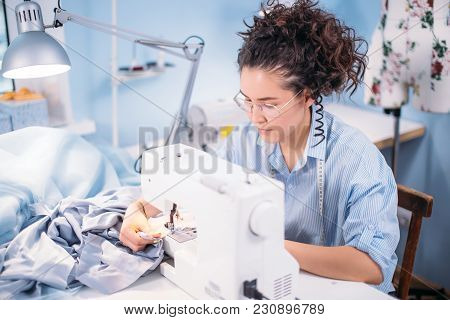 Nice Tailor With Curly Dark Hair Compliting Work With Sewing Machine At Workplace. Neatly Job. Crati