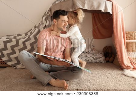 Father with little daughter reading bedtime story near hovel at home